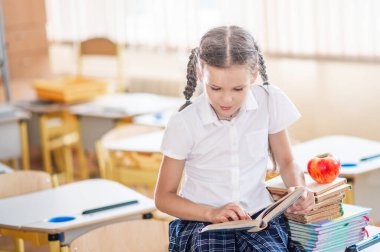 Okula dönecek olursak, birinci sınıf öğrencisi bir kız ders sırasında bir okul masasında otururken kitap okur. Bir liseli kız ders kitaplarını kullanarak ders çalışıyor. Okul malzemeleri bir çocuğun masasında..