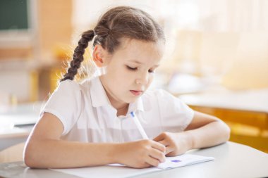 Okula geri dönmek, sınıftaki okul masasında oturan bir kız. Liseli bir kız ders veriyor ve bir deftere yazıyor. Okul malzemeleri çocukların masasında. Kız okul üniforması giyiyor..