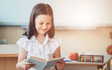 Okula dönecek olursak, birinci sınıf öğrencisi bir kız ders sırasında bir okul masasında otururken kitap okur. Bir liseli kız ders kitaplarını kullanarak ders çalışıyor. Okul malzemeleri bir çocuğun masasında..