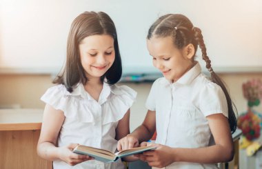 İki tatlı kız okul kitabı okuyorlar. Çocuklar yanlarında durur ve ellerinde bir kitap tutarlar. Okula dönelim. Öğrenciler kitap okuyor..