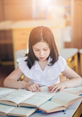 Okula dönecek olursak, birinci sınıf öğrencisi bir kız ders sırasında bir okul masasında otururken kitap okur. Bir liseli kız ders kitaplarını kullanarak ders çalışıyor. Okul malzemeleri bir çocuğun masasında..
