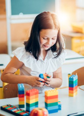 Okula geri dönmek, sınıftaki okul masasında oturan bir kız. Bir kız öğrenci geometrik şekilleri inceliyor - küp, piramit, top ve diğerleri. Okul malzemeleri bir çocuğun masasında..