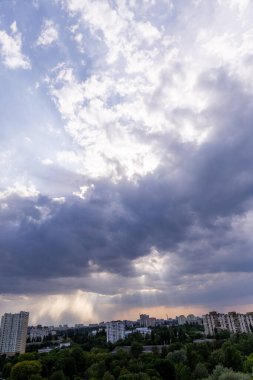 Devasa, dinamik bulutlar canlı bir metropolün üzerinde gökyüzünde dönüyor. Altın ışınlar parlamaya çalışırken dramatik gölgeler bırakıyor. Sakin ve öngörülü bir atmosfer hakim olur..