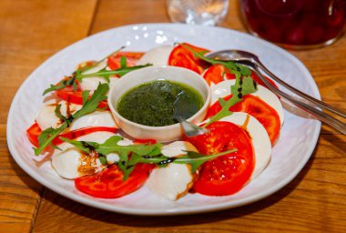 Canlı mozzarella dilimleri ve olgun domatesler bir tabağa güzelce yerleştirilmiş fesleğen sosu serpiştirilmiş ve üzerine taze roka serpiştirilmiş..