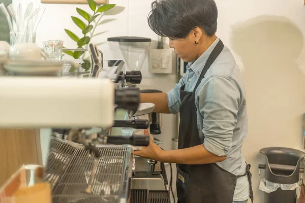 緑のコーヒーショップでお客様のためにホットドリンクを準備しているアジアの女性バリスタ カウンターの後ろにコーヒーカップを準備するためにコーヒーマシンと一緒に働く若いバリスタ — ストック写真