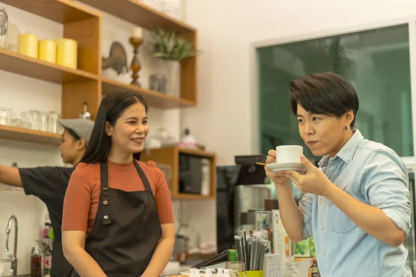 Female customer is happy to take a taste of fresh hot coffee from a young shop owner. Lady with warm hospitality and care hands a cup of hot drink to her client