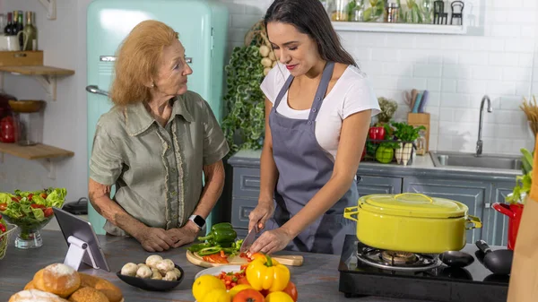 Elderly mother and young daughter getting online cooking class to prepare meal at home. Good family relationship between mom and daughter cooking together