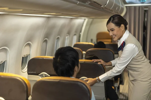 Young attractive female airline crew or attendant is helping passenger to feel comfortable while sitting in an airplane cabin. Hospitality and service mind from airline stewardess on a flight.