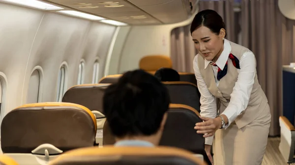 Young attractive female airline crew or attendant is helping passenger to feel comfortable while sitting in an airplane cabin. Hospitality and service mind from airline stewardess on a flight.