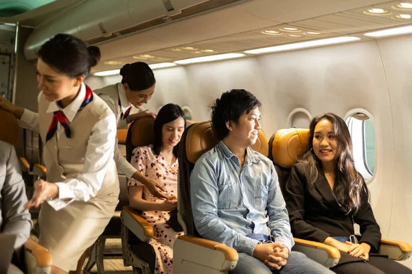 Young couple passengers enjoy taking economic seats with support from a female airline attendant while waiting to take off their flight. People feel comfortable and relax sitting in an airplane cabin