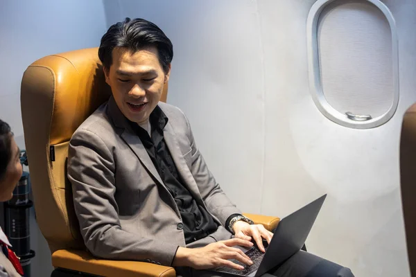 Young Asian male businessman uses mobile phone to connect with his colleague while siting in an airplane cabin before boarding