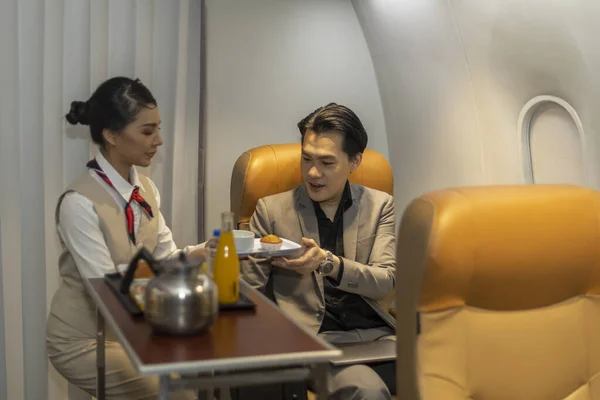 Female airline stewardess or attendant serves her male customer with refreshment and snake during the flight. Inflight service for business class passenger