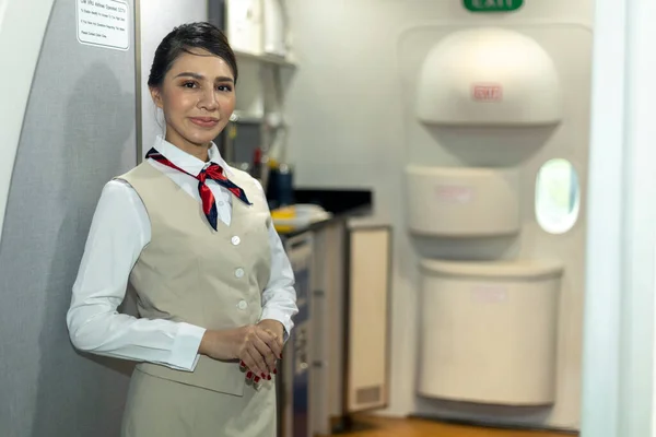 Young attractive airline attendant or stewardess is welcoming passengers to the flight at the airplane door. Hand gesture to ease customer or client