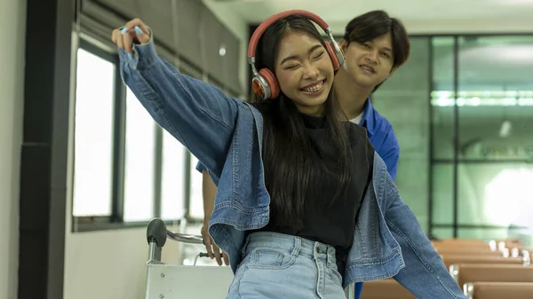 stock image Young teenager couple enjoys listening music with wireless headset and shows happiness while waiting for boarding at a terminal lounge