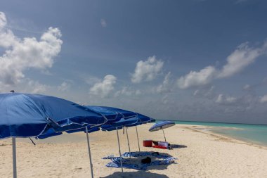 Sahil şemsiyeleri turistler için mavi gökyüzü arka planına sahip temiz ve sessiz bir kumsalda bir arada duruyorlar..