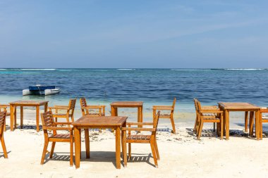 Yemek masaları ve sandalyeler temiz ve sessiz kumsalda, derin mavi denizin yanında.