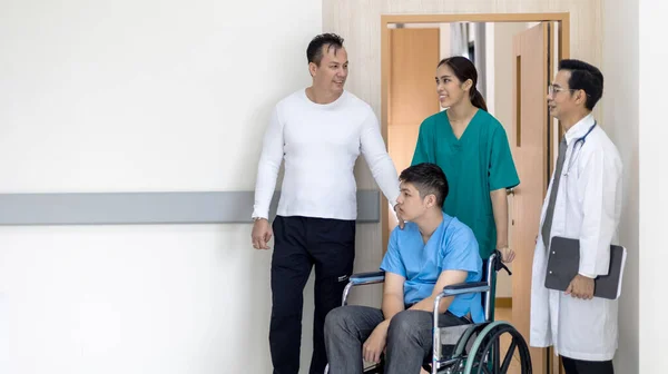 若い男の子障害の患者は 病院の廊下を移動するために看護師や医師のサポートの下の車椅子に座っています ストック写真