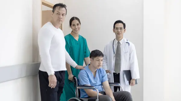 若い男の子障害の患者は 病院の廊下を移動するために看護師や医師のサポートの下の車椅子に座っています ロイヤリティフリーのストック写真