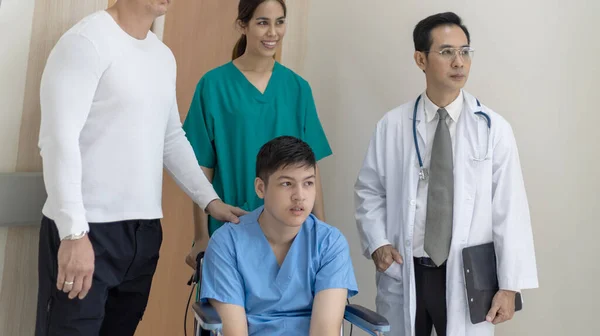若い男の子障害の患者は 病院の廊下を移動するために看護師や医師のサポートの下の車椅子に座っています ストック画像