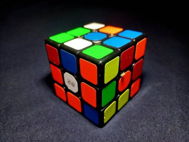 A Rubik's Cube positioned against a stark black backdrop, viewed from the side. clipart