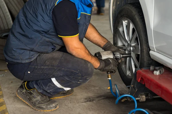 Stock image Auto mechanic man with electric screwdriver changing tire outside. Car service. Tire installation concept. High quality photo