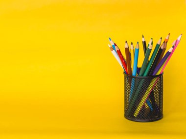 Silindir şeklinde metal ağ kalem tutacağı sarı arka planda izole edilmiş. Birçok renkli kalem, eğitim konsepti, kopyalama alanı. Yüksek kalite fotoğraf