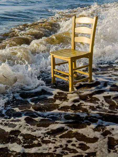 Single wooden yellow chair among the waves on the beach. High quality photo
