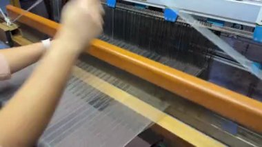 Sanayi tekstil fabrikası. Dokuma tezgahında ilerleyen kalın beyaz iplikçikleri kapatın. Geleneksel dokuma tezgahında üretim yapan kadın.