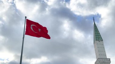 Cami minaresinin yanında mavi gökyüzünde dalgalanan Türk bayrağı. Türkiye Cumhuriyeti ulusal kırmızı işareti. Bayrak direğinde kırmızı bayrak sallanıyor. 