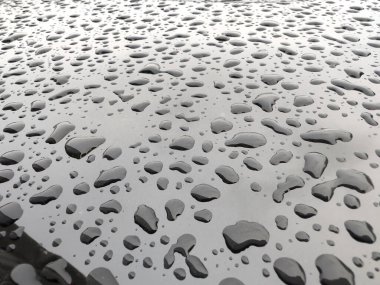 Yağmur damlalarıyla kaplı siyah bir yüzeye yakından bakmak yüzeyin dokusunu ve parlayan su damlacıklarını ortaya çıkarır..