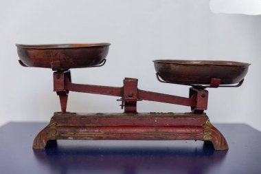 Antika denge ölçeğinde iki bakır tava ve antika tartma aletlerinin zarafetini vurgulayan güzel işlenmiş bir kırmızı taban bulunuyor..