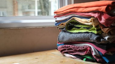 Ahşap masada bir yığın elbise ve arka planda bir pencere. Temiz katlanmış pamuklu kotlar, renkli tişörtler. Ev işi, ütü, bakım ve eşya depolama kavramı. Boşluğu kopyala