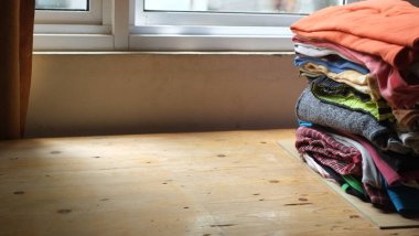 Ahşap masada bir yığın elbise ve arka planda bir pencere. Temiz katlanmış pamuklu kotlar, renkli tişörtler. Ev işi, ütü, bakım ve eşya depolama kavramı. Boşluğu kopyala