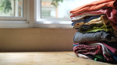 Ahşap masada bir yığın elbise ve arka planda bir pencere. Temiz katlanmış pamuklu kotlar, renkli tişörtler. Ev işi, ütü, bakım ve eşya depolama kavramı. Boşluğu kopyala