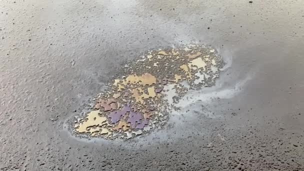アスファルトのガソリン色のスポットでプリドルに雨が降る — ストック動画