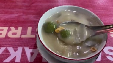 Endonezyalı bir adam beyaz bir kase içinde sıcak bir wedang ronde karıştırıyor. Wedang ronde, tangyuan veya glutinous tatlısı, zencefilli şurupta servis edilir ve kızarmış fıstıkla karıştırılır..