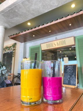 Meyve suyunun ahşap masasında iki büyük bardak ejderha meyvesi ve mango suyu. 