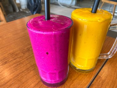 Meyve suyunun ahşap masasında iki büyük bardak ejderha meyvesi ve mango suyu.