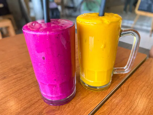 Meyve suyunun ahşap masasında iki büyük bardak ejderha meyvesi ve mango suyu.