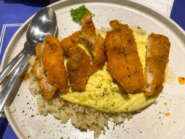 Tereyağlı pilav ve kızarmış yumurta ile servis edilen tavuk göğsü şnitzel.