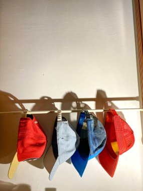 Beyzbol şapkası beyaz direkte asılı. Duvarında gölgeleri olan çeşitli renkli şapkalar..