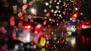 Yağmurlu Gece Yolu: Kırmızı Bokeh ve Damlacıklar arabanın ön camında. Dağınık araçlar yağmurda camları aydınlatıyor.