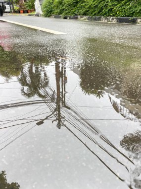 Asfalt yolda su birikintisine yansıyan elektrik hatları.