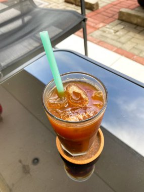 Bir bardak siyah buzlu kahve cam bir masanın üzerinde pilavdan yapılmış mavi bir pipet.