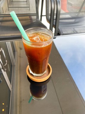 Bir bardak siyah buzlu kahve cam bir masanın üzerinde pilavdan yapılmış mavi bir pipet.