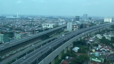 Tren ve arabalar yüksek paralı yolda ve şehirde yavaşça ilerliyorlar. Etrafında binalar varken, gün ışığında yüksek açı., 