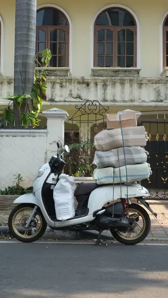 Motosikletli gezintiler ve konut alanına aşırı yüklü bir scooter park etmek. Kuryelerle mal taşımak ve teslimat yapmak için motosiklet kullanımı Endonezya 'da yaygındır..