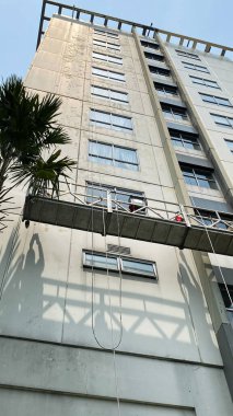 İşçiler bir binadaki gondolda çalışıyorlar. İki işçi, önleyici bakım ve onarım tedbiri olarak gökdelen pencerelerine erişim ve temiz cam pencereler için özel ekipman kullanıyor