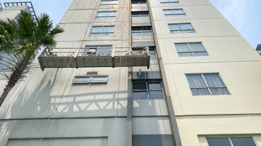 İşçiler bir binadaki gondolda çalışıyorlar. İki işçi, önleyici bakım ve onarım tedbiri olarak gökdelen pencerelerine erişim ve temiz cam pencereler için özel ekipman kullanıyor