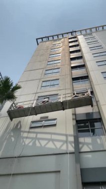 İşçiler bir binadaki gondolda çalışıyorlar. İki işçi, önleyici bakım ve onarım tedbiri olarak gökdelen pencerelerine erişim ve temiz cam pencereler için özel ekipman kullanıyor